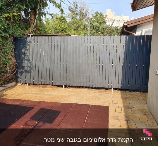גדר עץ אפורה בחצר עם ריצוף אבן
